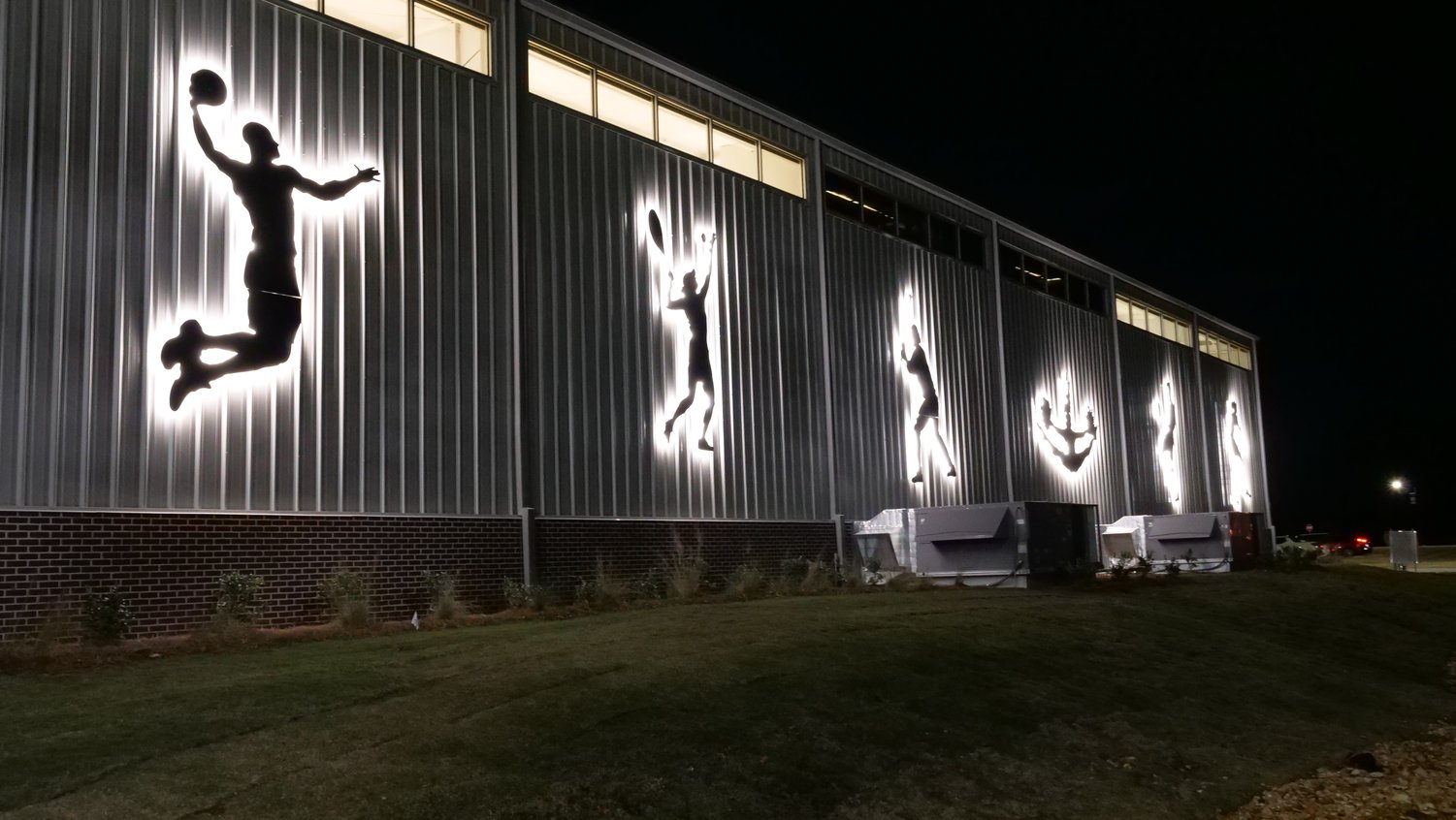 Illuminated athlete silhouettes on the exterior of the Henderson Park recreation facility at night.