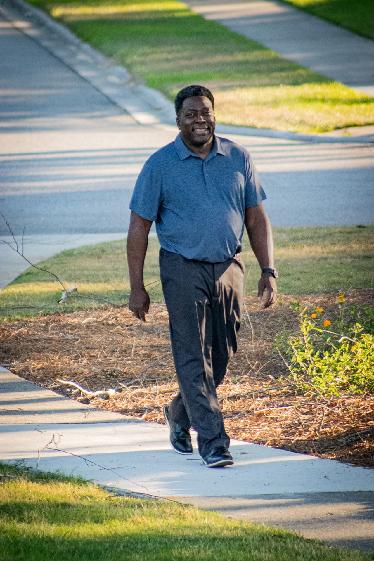 Dave London walking along a neighborhood sidewalk in evening light.